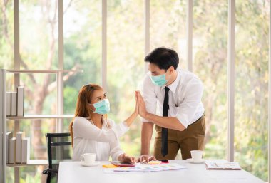 Ofiste mutlu bir şekilde gülümseyen, cerrahi maske takan iş arkadaşları, virüsten korunuyor.