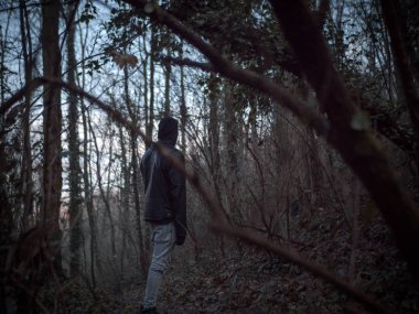 Hood ve deri ceket ile genç adam Bergamo, milano karanlık orman bakar