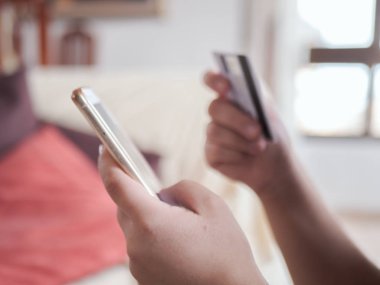 Genç kadın oturma odasından kredi kartı ile akıllı telefon ile online satın alır.