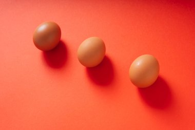 Kırmızı arkaplanda üç kahverengi tavuk yumurtası var..
