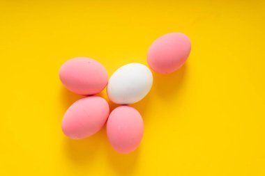 Sarı arka planda beyaz ve pembe yumurtaların üst görüntüsü. Renkli yumurtalar.