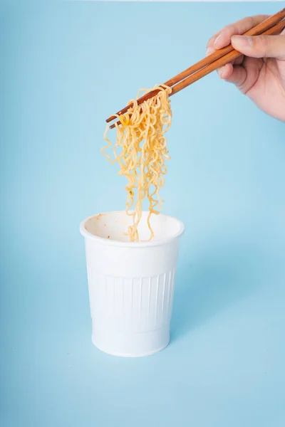 用木制筷子从蓝色背景的杯子里吃方便面的人的手 — 图库照片