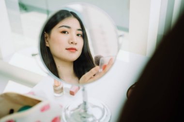 Güzel Asyalı genç Taylandlı kadın. Uzun siyah saçlı. Evinde aynanın önünde makyaj yapıyor..