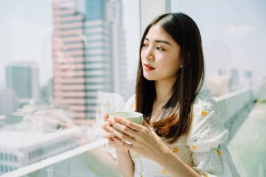 Güzel Asyalı genç Taylandlı kadın. Uzun siyah saçlı. Bir fincan çay, kahve. Evde içmenin tadını çıkar..