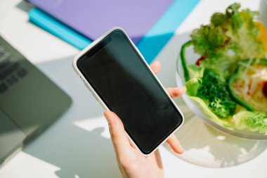 Uzayı kopyala Ofisteki kadın eli ve salata yayında akıllı telefon..