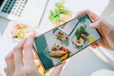 Çalışan ofis masasında akıllı telefonuyla sağlıklı yiyeceğin fotoğrafını çeken kadının en iyi görüntüsü. Boşluğu kopyala.