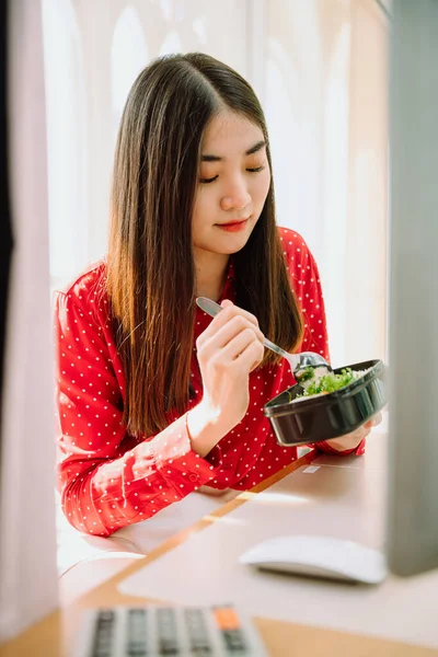 아름다운 아시아인의 여인붉은 셔츠를 집에서 컴퓨터 앞에서 일하는 음식을 있었다 — 스톡 사진