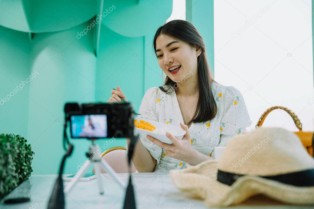 Food blogger and vlogger. Cheerful beautiful asian thai woman review mango sticky rice in front of camera.