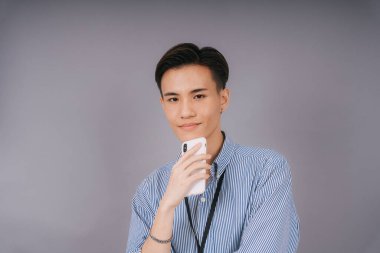 Mavi yaka gömlekli yakışıklı Taylandlı işadamı akıllı telefonu kendine güvenle tutuyor. ticari kullanım.