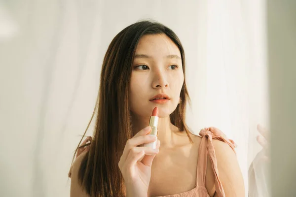 美しいタイのアジアの女性は 白い部屋の中に口紅の化粧品を保持 日当たりの良い暖かい光 — ストック写真