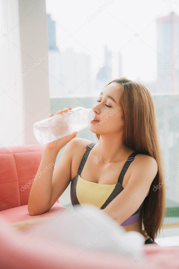 Beautiful woman in sportwear with natural make up isolated over white background. Healthy woman in sportbra enjoy drinking from ice cold bottle of water after work out. Quarantine at home.