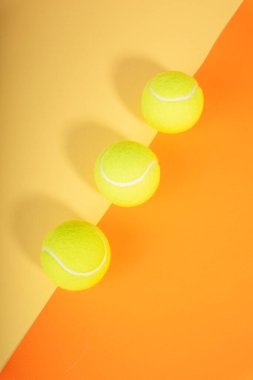 Turuncu ve sarı kortun üzerinde üç tenis topu. Üst Manzara. Düz yatıyordu.