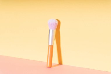 Parlak sarı arka planda makyaj fırçası kozmetik gerekliliği.