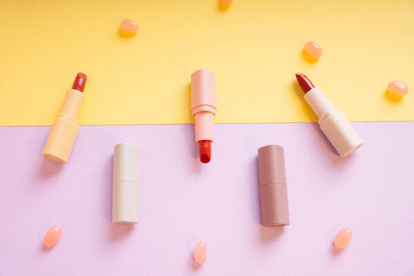 Red lipsticks on yellow and purple background and candy. Top view. Flat lay.