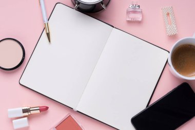 Üst görünüm - Kozmetik makyaj araçları ve pembe masadaki akıllı telefonlu boş kitap.