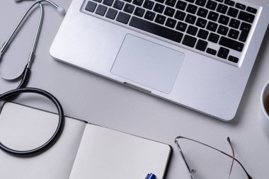 Üst görünüm - Doktor stetoskop, laptop, kitap ve gözlüklü çalışma masası.