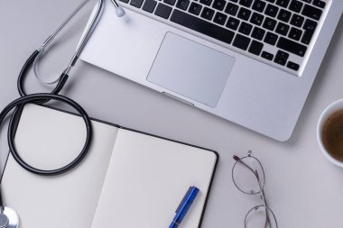 Üst görünüm - Doktor stetoskop, laptop, kitap ve gözlüklü çalışma masası.