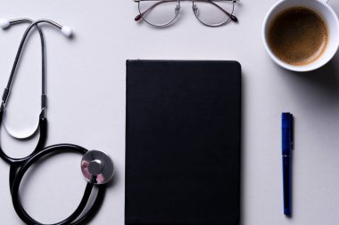 Üst görünüm - Doktor çalışma masası steteskop, tablet, kalem ve gözlüklü gri arkaplan üzerinde.