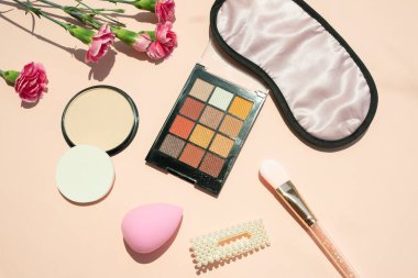 Pembe arka planda izole edilmiş dekoratif ürünler. Çiçekler, kozmetik palet, pudra pudrası, sünger, fırça. Üst görünüm.