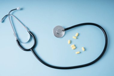 Doktor geçmişi - Steteskop ve ilaç hapları mavi arka planda.