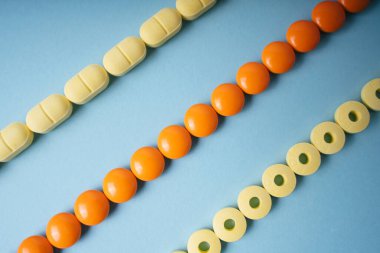 Sarı ve turuncu ilaç hapları mavi arka planda hizada..