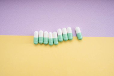 Beyaz ve açık yeşil ilaç kapsülü sarı ve mor arka plan üzerinde.