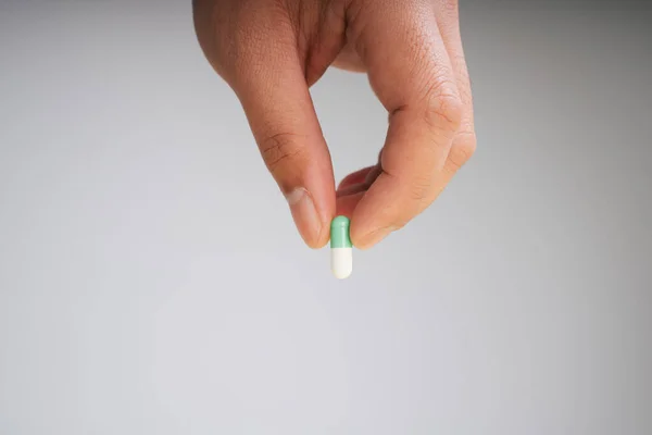 Human hand picking up medicine drug capsule isolate over grey background.
