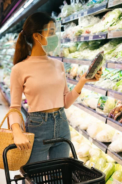 New normal life - Asian thai woman wearing face shield and mask shopping in supermarket. Selecting ingredient on a shelf.