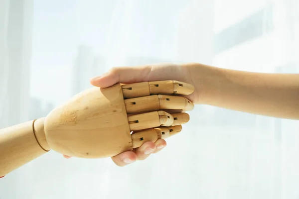 Hand of wooden cyborg robot and human shaking hand.