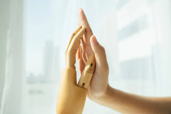 Hand of wooden cyborg robot and human touching each other.