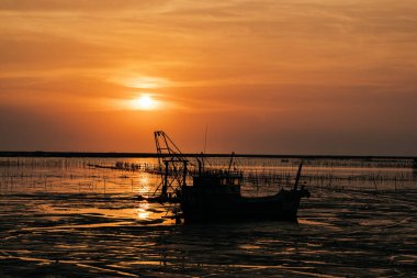 Yatay siluet çekim. Deniz yüzeyinde balıkçı teknesiyle gün batımı manzarası.