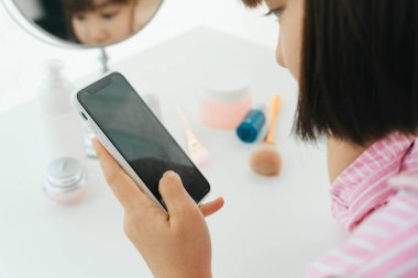 Genç ve güzel Asyalı Taylandlı siyah kısa saçlı kadın tuvalette akıllı telefon kullanıyor..