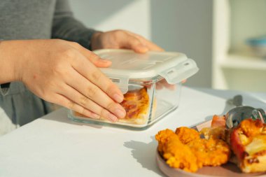 Kadehi tutan kadın içinde pizza dilimi olan bir kutu taşıyor..