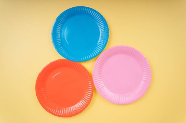 Sarı bej arka planda dört renkli plastik tabak. Turuncu. Mavi. Pembe..