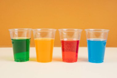 Tatlı gökkuşağı soda, fotokopi alanı olan plastik bardakta köpüklü su. Yeşil. Mavi. Turuncu. Kırmızı.