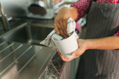 Hizmetçi kadın mutfakta bez parçasıyla bardak seramiğini temizliyor. Covid-19 Coronavirus önleme.