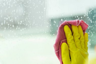 Hizmetçi sarı eldiven giyip pembe bez bezle aynayı temizliyor. Covid-19 Coronavirus önleme.