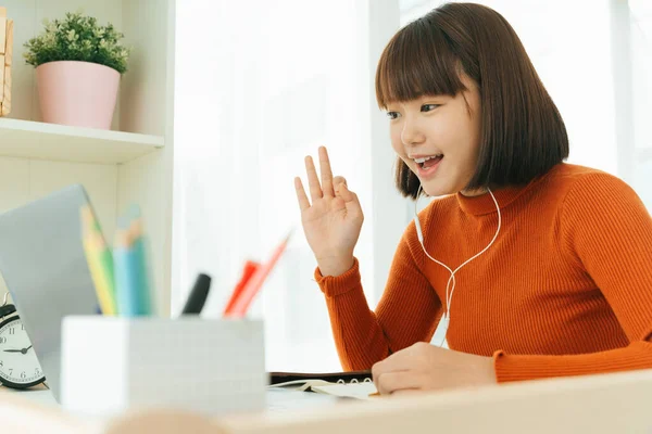 Genç Asyalı güzel, kısa saçlı, kısa saçlı, kısa saçlı, ev ödevini laptopta öğrenen ve kulaklık takan bir kadın. Tamam..