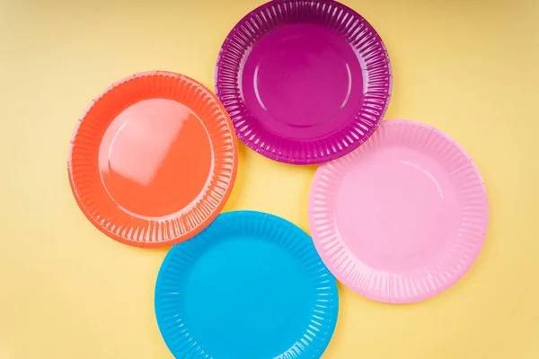 Four colourful plastic plate dishes over yellow beige background. Orange. Purple. Blue. Pink.