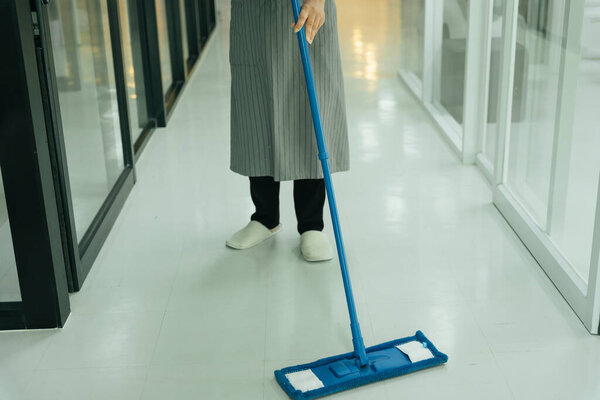 Maid using mop cleaning the floor in condo apartment room.
