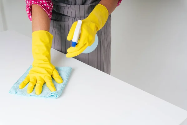 Temizlikçi kadın eldiven giyip yemek masasını bez bez ve deterjan şişesiyle temizliyor. Covid-19 Coronavirus önleme.