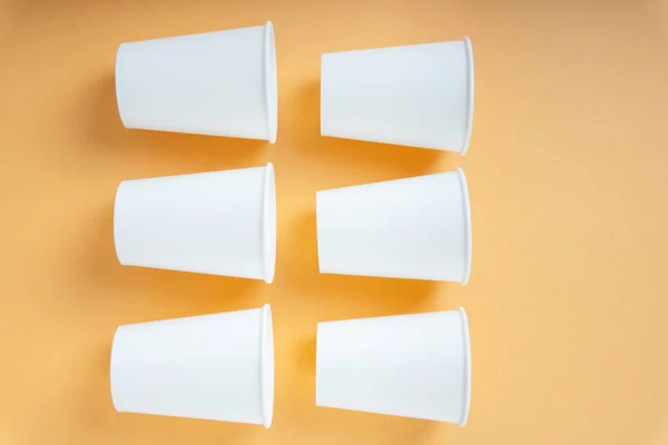 Six paper cups in square shape laying over orange background.