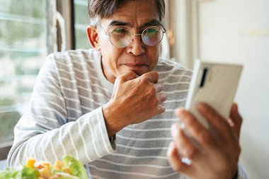 Gözlüklü yaşlı adam gülümserken çocuğuyla telefon görüşmesini akıllı telefondan yapıyor..