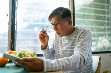 Yaşlı adam akıllı telefonu çalarken gözlük takmaya çalışıyor..