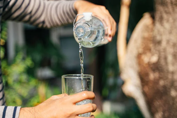 Bir adam şişeden temiz içme suyunu yatay olarak bardağa dökerken bir şişe ve bardağın kırpılmış görüntüsü..