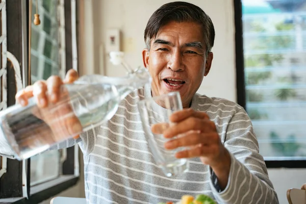 Old man hold the glass and bottle of water in his hands, he will pour the drinking water into the glass.