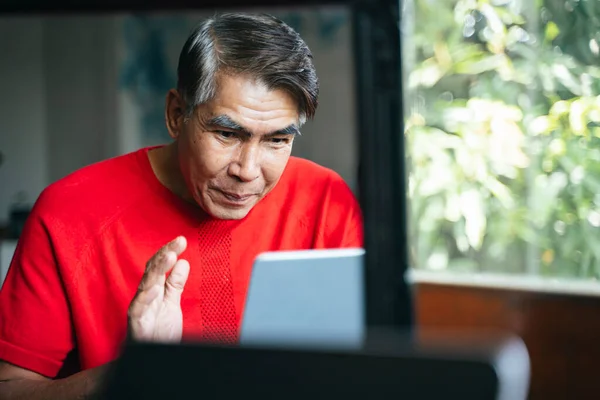 Reflection in a mirror of old man while he use tablet for social media.