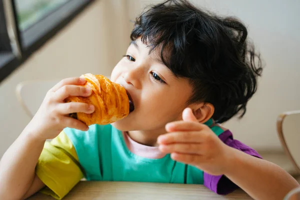 Kisfiú Harapni Enni Kolbász Croissant Finoman Reggeli Konyhában — Stock Fotó