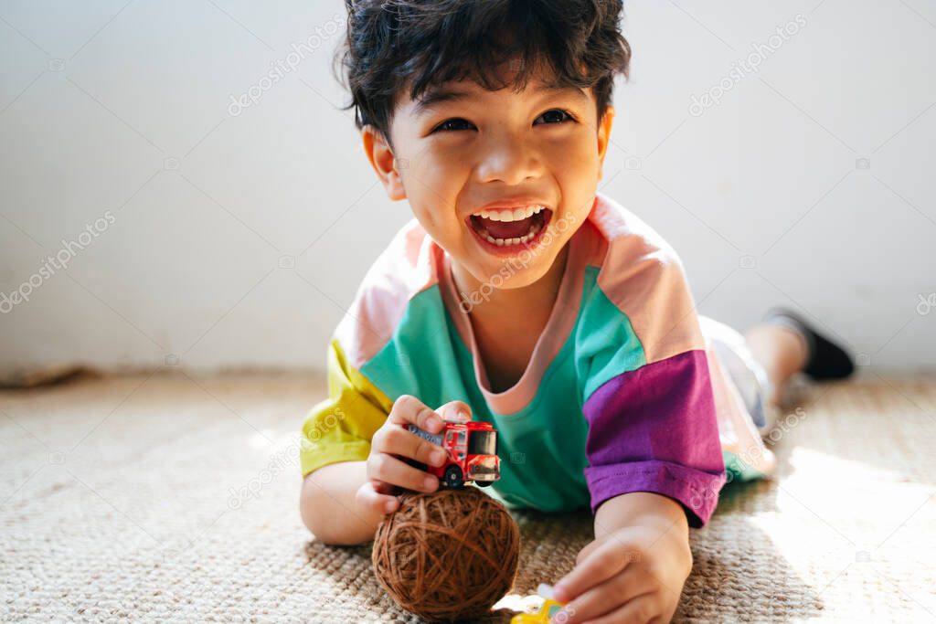 Little boy lie down on the stomach on the floor and playing car toy.