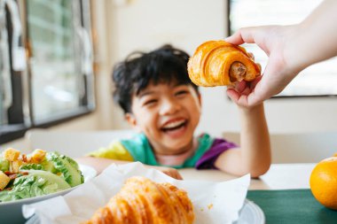 Küçük çocuğun ailesinin elinden aldığı sosisli kruvasanın kesilmiş görüntüsü..